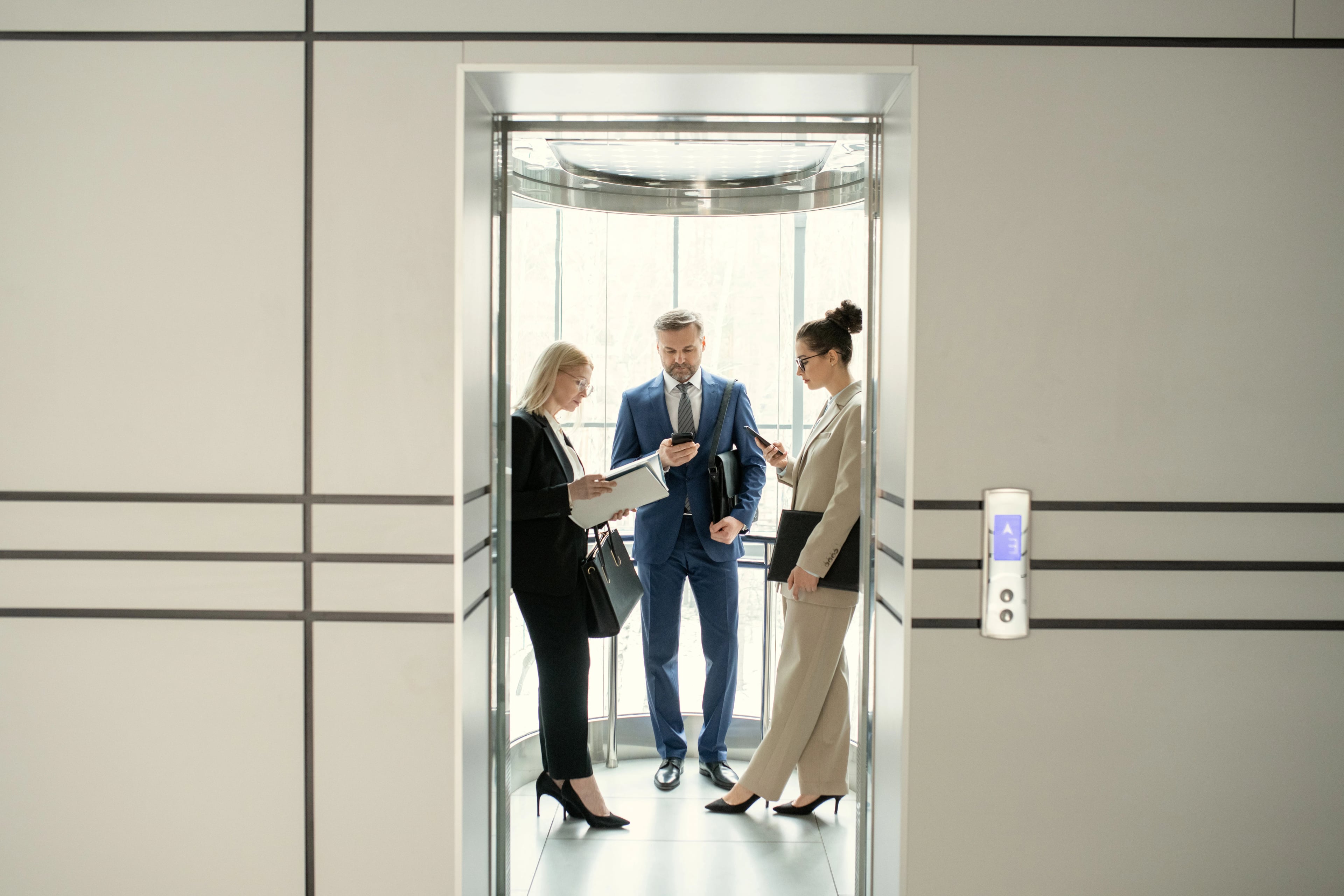Trois professionnels en tenue de bureau discutant dans une cabine d'ascenseur panoramique ouverte