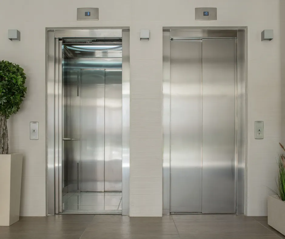 Deux ascenseurs en acier inoxydable côte à côte dont un ouvert dans un hall lumineux avec plantes