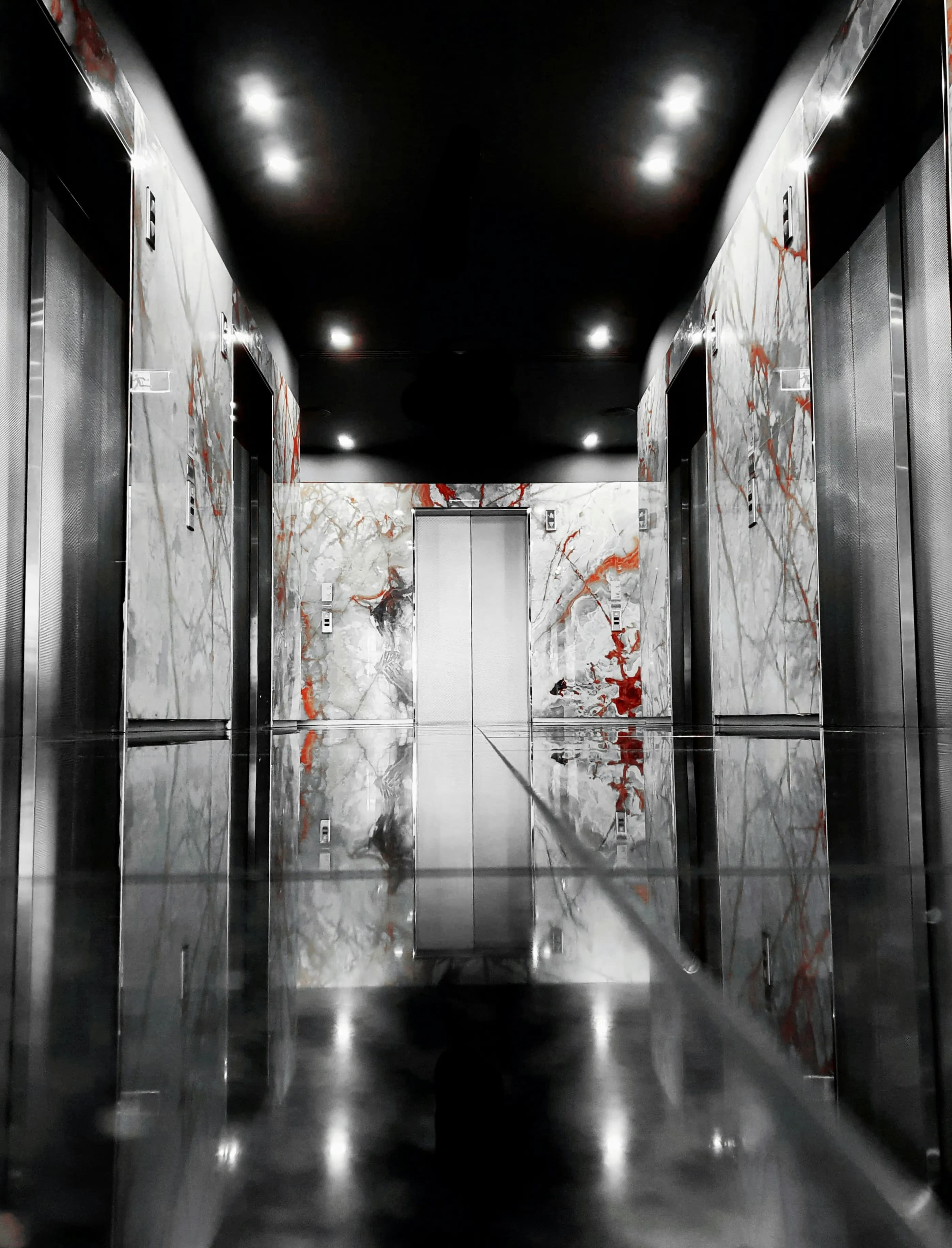 Hall luxueux avec plusieurs cabines d'ascenseur aux portes métalliques sur fond de mur en marbre blanc et rouge