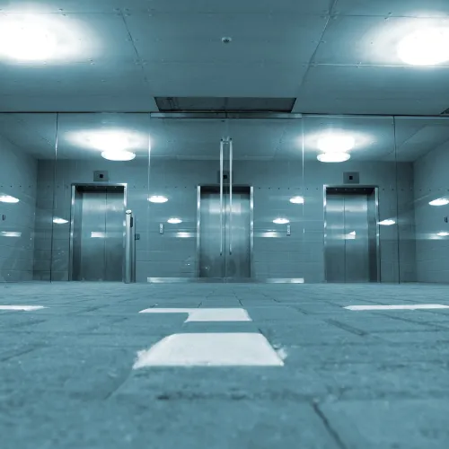 Hall industriel avec trois cabines d'ascenseur aux portes en acier inoxydable sous éclairage bleuté