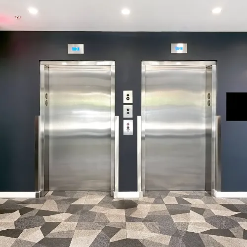 Deux ascenseurs côte à côte avec portes en acier poli dans un couloir aux murs sombres