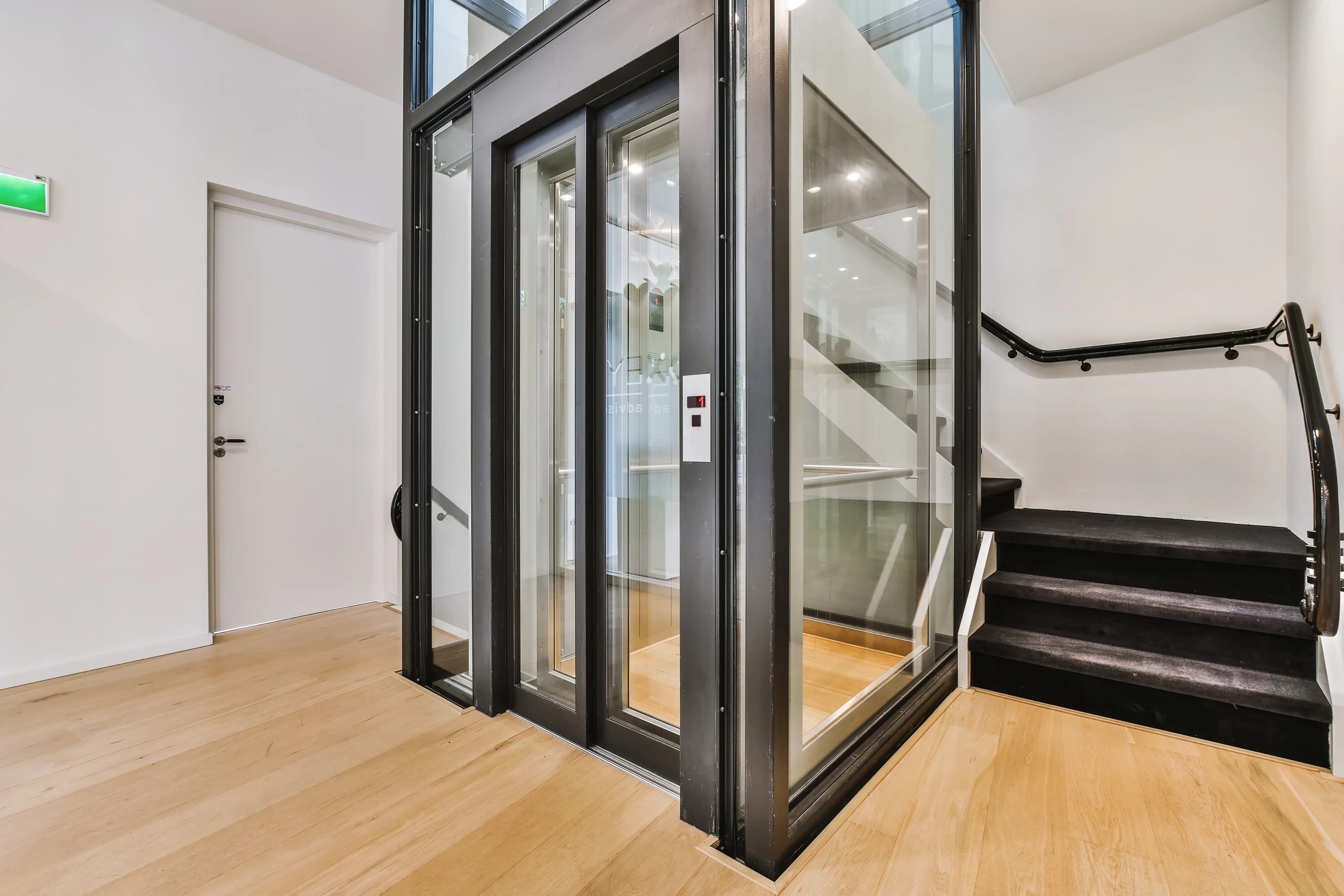Ascenseur résidentiel vitré avec structure en aluminium noir installé à côté d'un escalier moderne